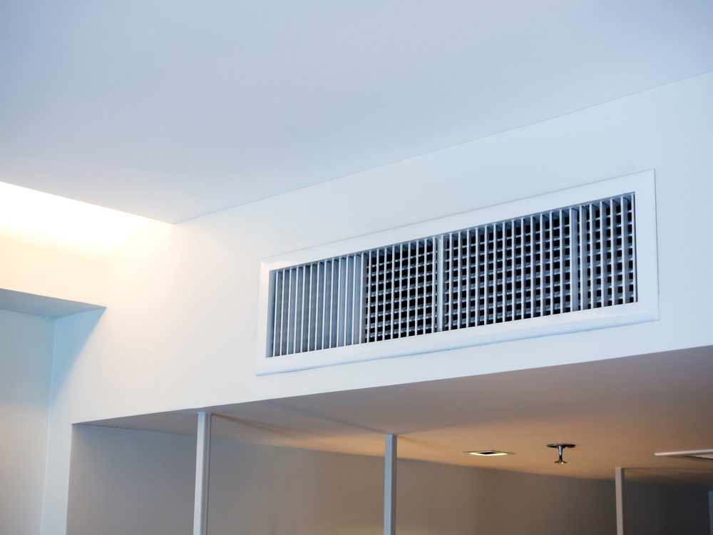 A white ceiling with a large rectangular air vent. Natural light comes from the left, and recessed lighting is visible on the ceiling. The walls are light-colored, and the overall setting appears modern and minimalistic.