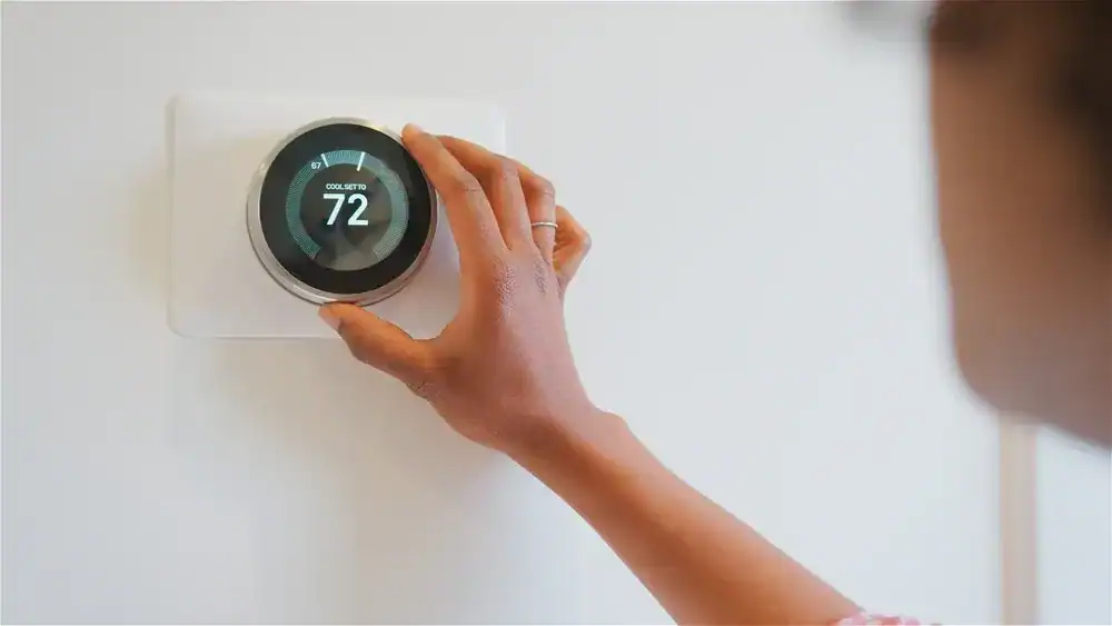 A person adjusts a smart thermostat on a white wall, setting the temperature to 72 degrees—a service often recommended by an HVAC Contractor in Nassau County, NY. The hand is in focus, with the face blurred in the foreground.