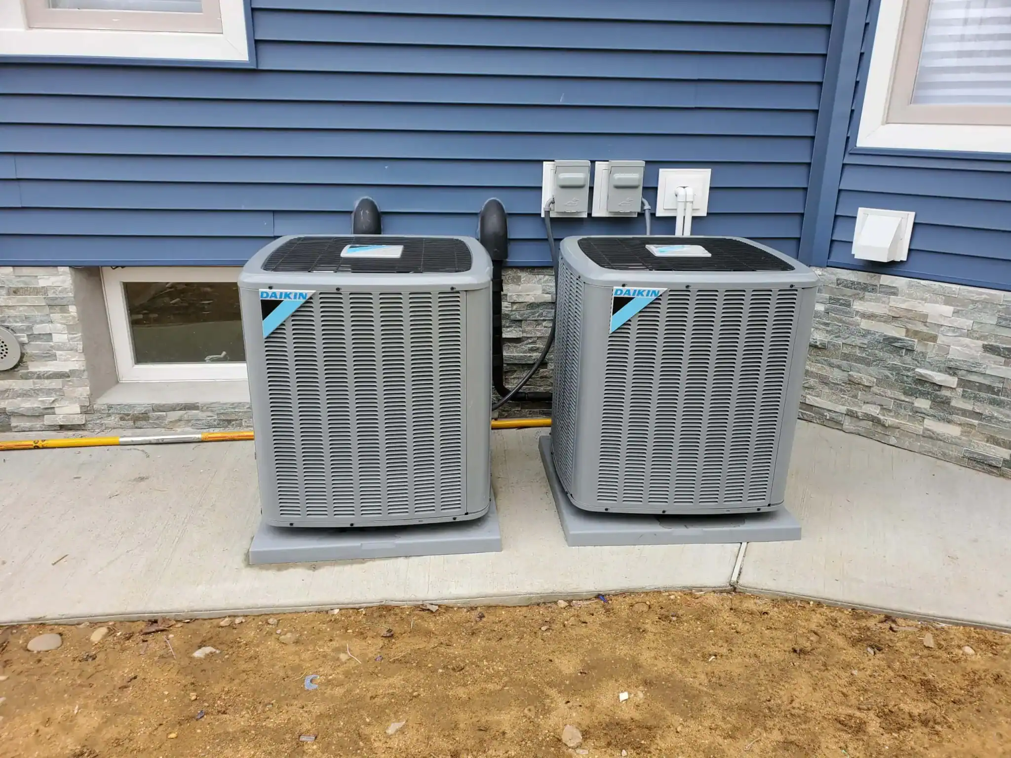 Two outdoor air conditioning units installed beside a house.