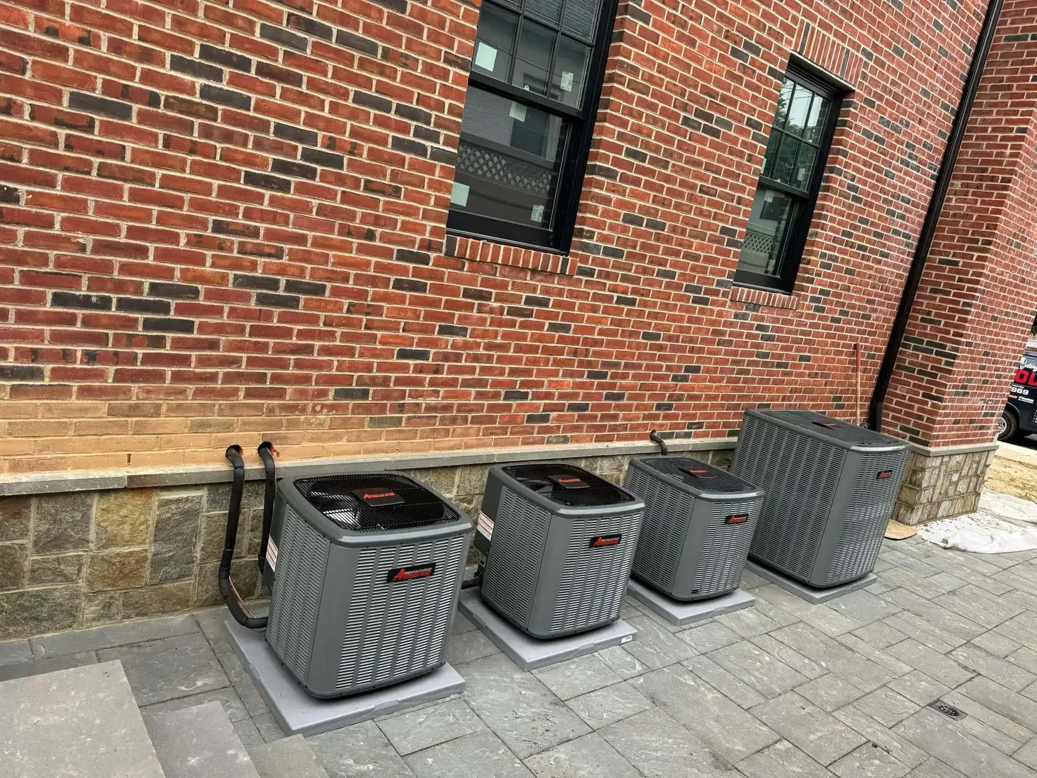 Four HVAC units installed outside a brick building.