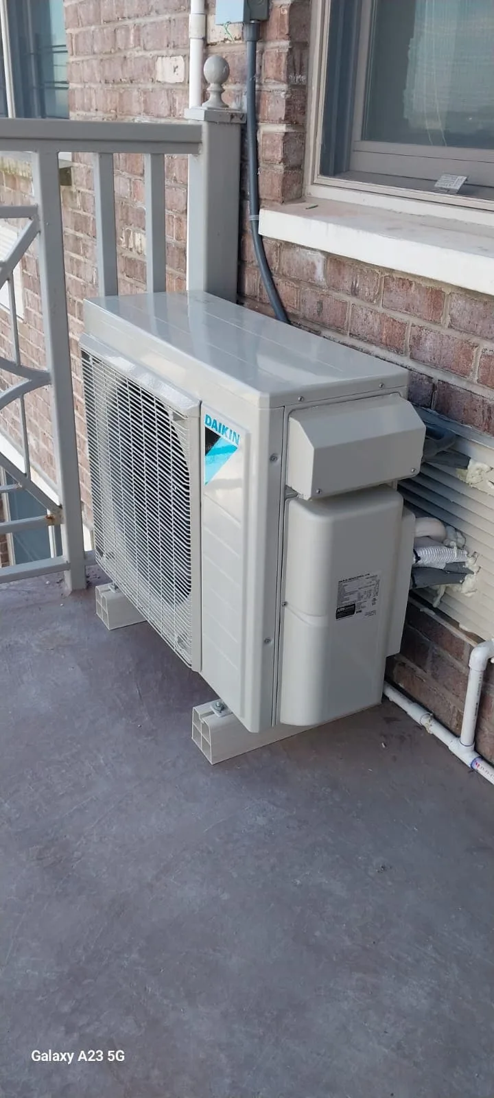 Daikin air conditioning unit mounted on a balcony next to a brick wall.