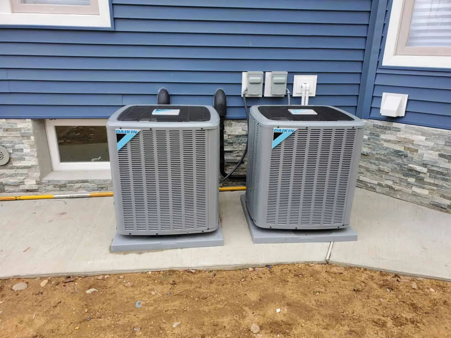 Two Daikin air conditioning units outside a blue sided home.