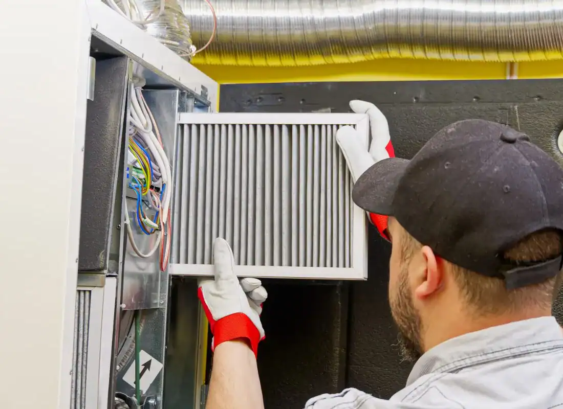 Technician wearing gloves installs air filter in HVAC system.