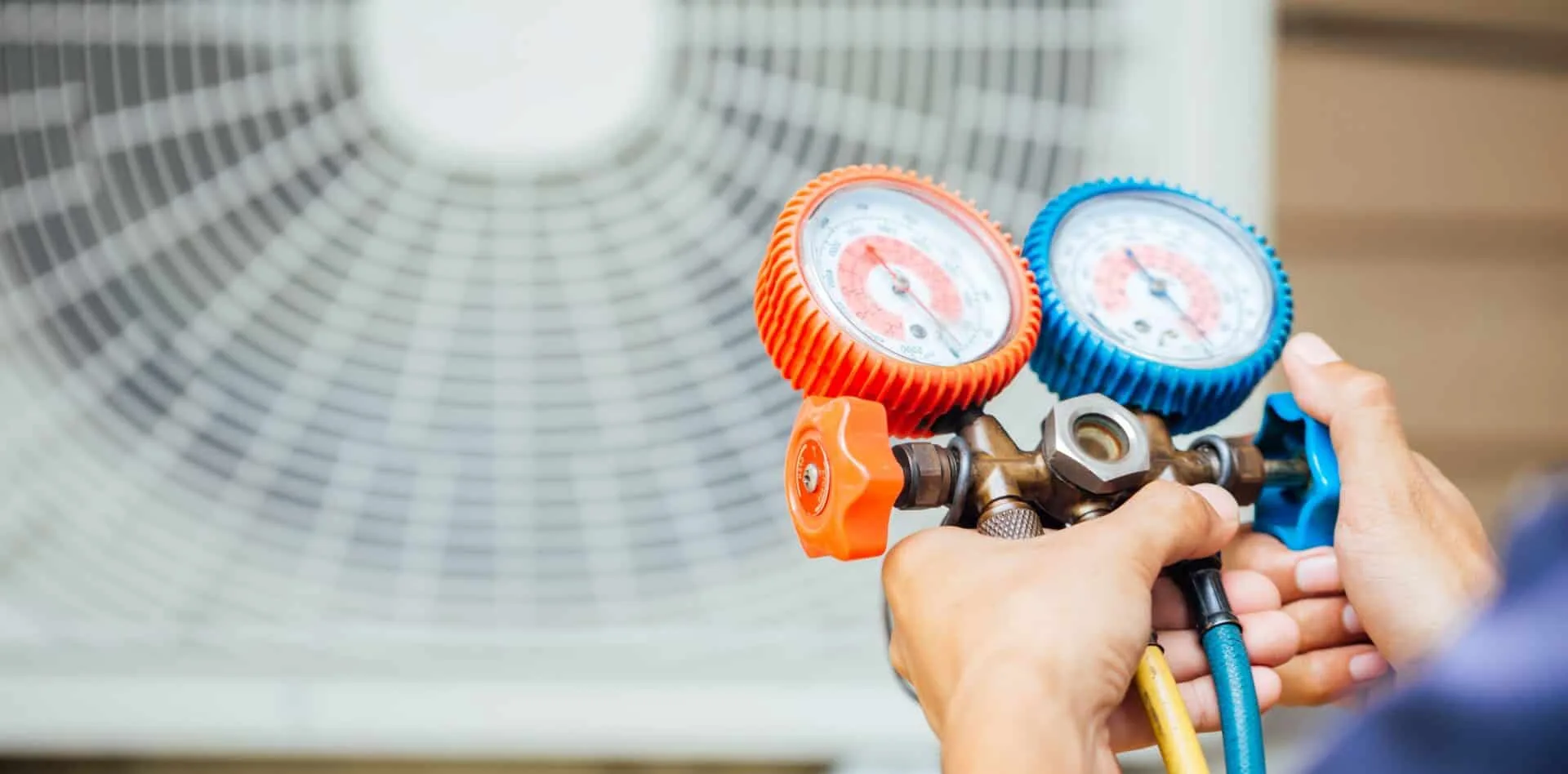 Hands adjusting pressure gauges on an HVAC system with fan in background.