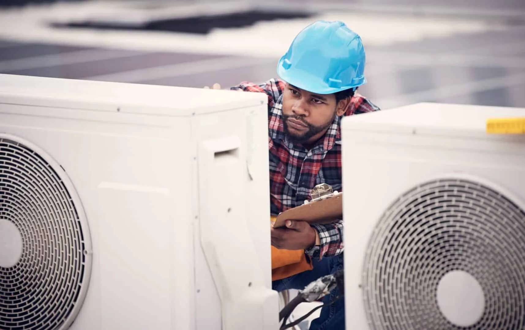 HVAC technician in blue helmet inspecting outdoor air conditioning units.