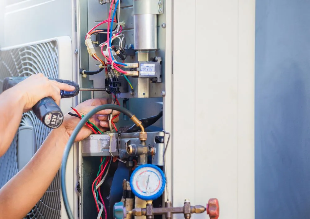 Technician using tools to repair an air conditioning unit with exposed wires.