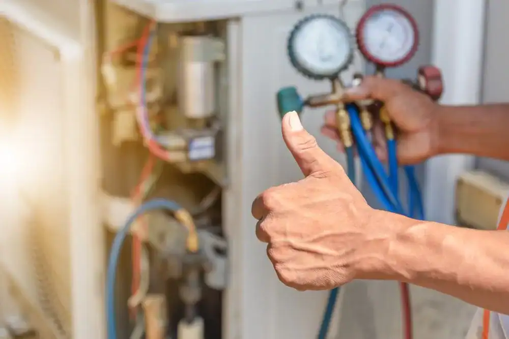HVAC technician showing thumbs up while servicing unit with gauges.