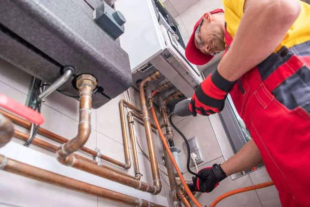 Plumber in red uniform working on a boiler installation with copper pipes.