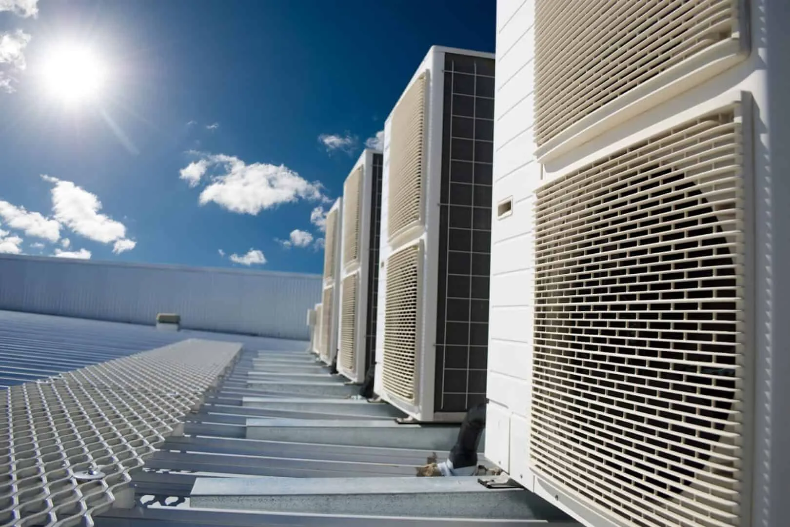 Rooftop HVAC units against a clear blue sky with sunlight and clouds.
