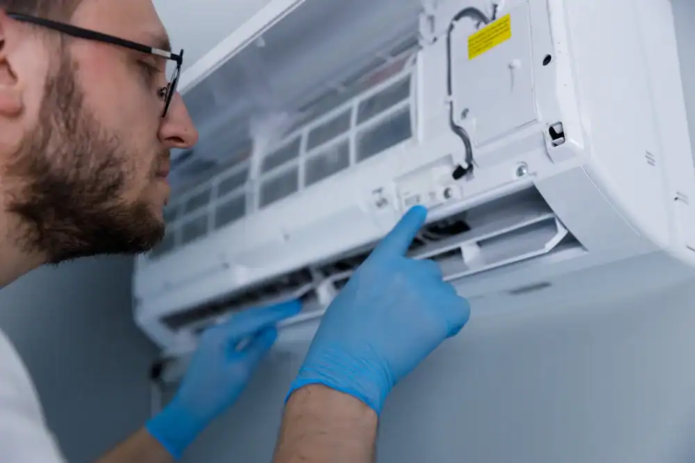 Technician in blue gloves checking a wall-mounted air conditioning unit.