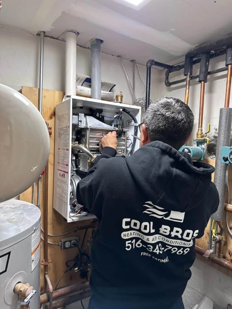 Technician in black hoodie working on an HVAC boiler system in a basement.