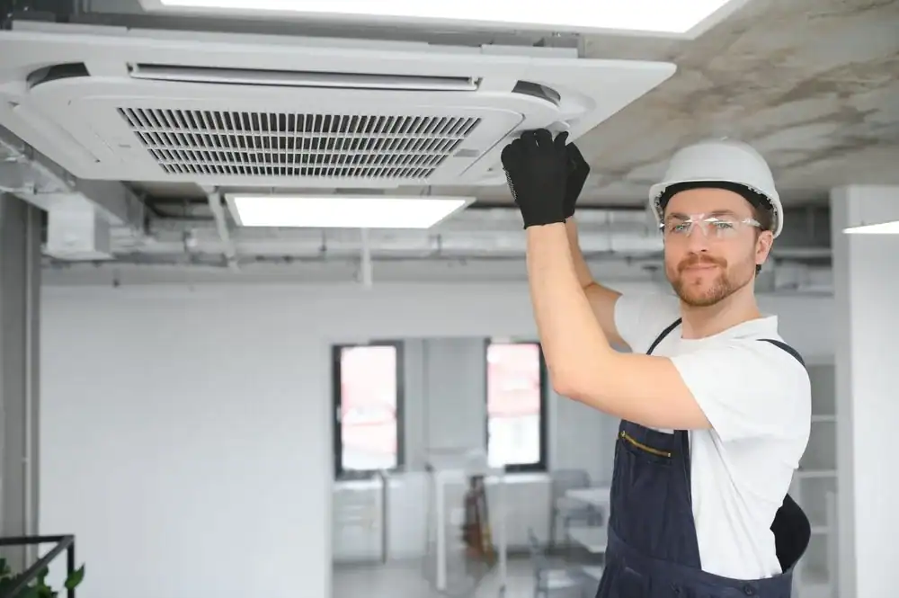 Technician in uniform installing a ceiling air conditioning unit.