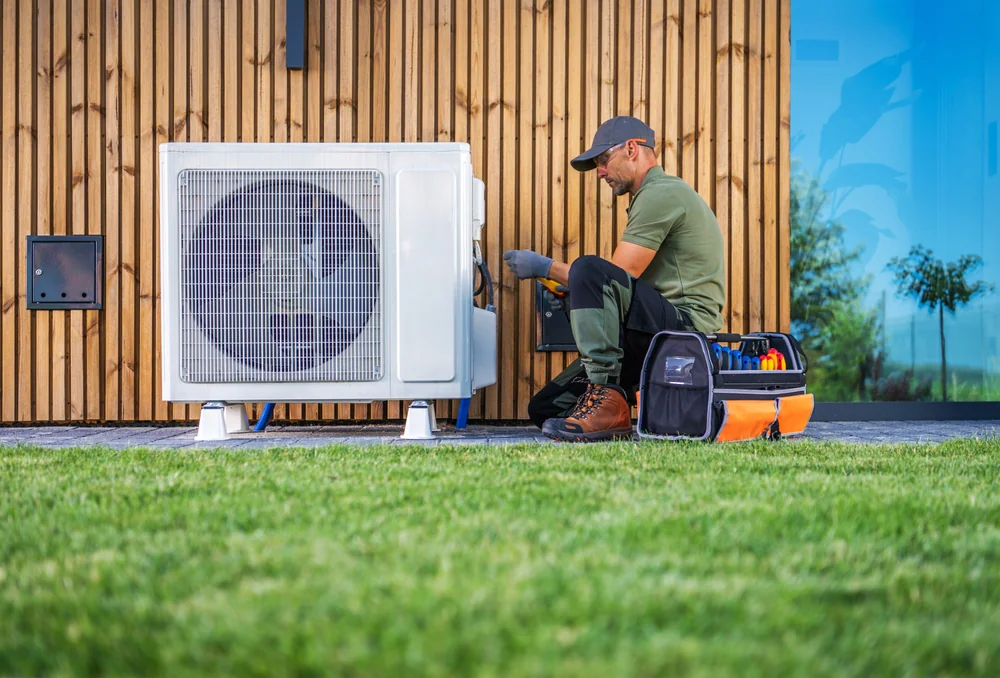 A technician repairs an outdoor HVAC unit next to a wooden wall.