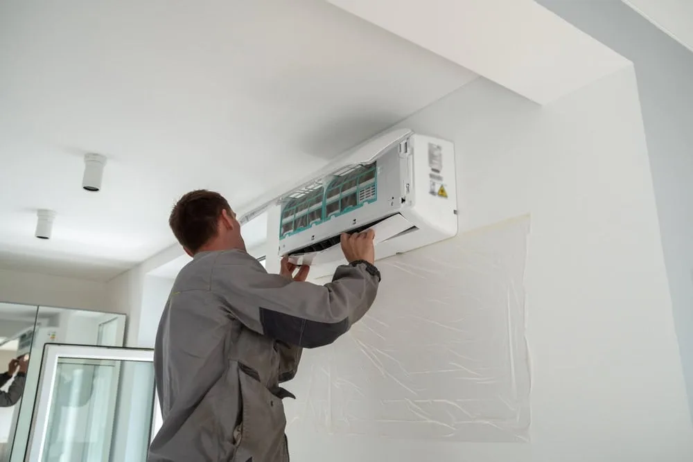 Technician in gray uniform installing air conditioning unit on wall.