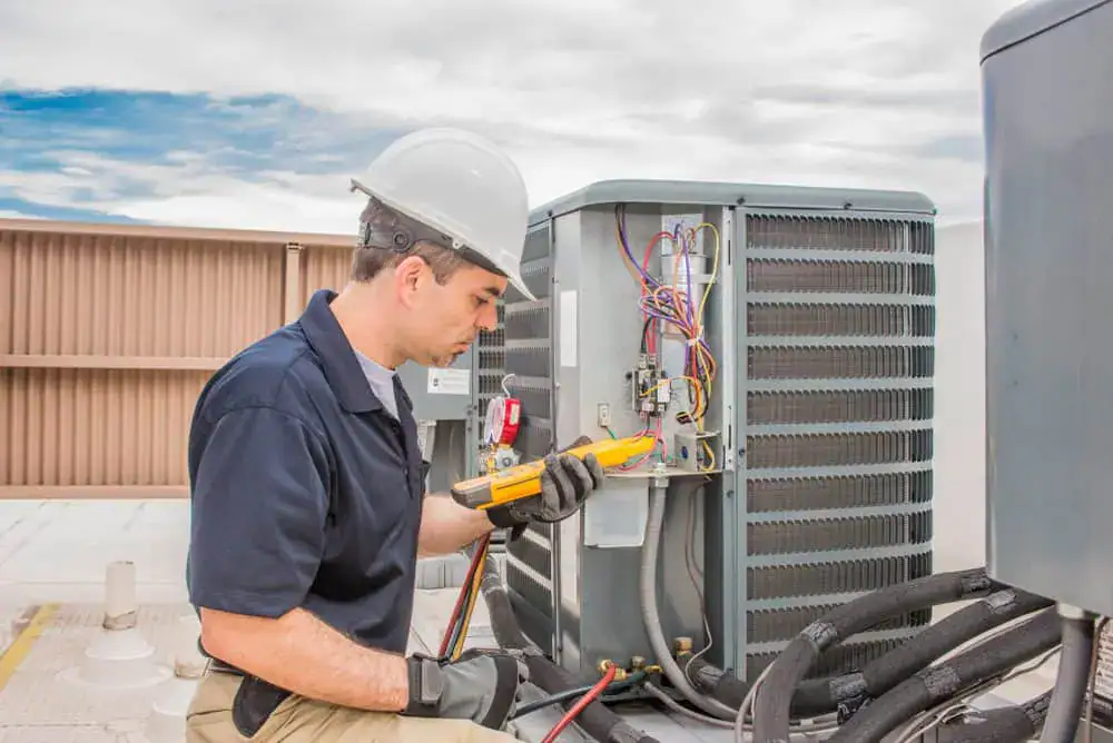 HVAC technician in hard hat repairing rooftop air conditioning unit using tools.